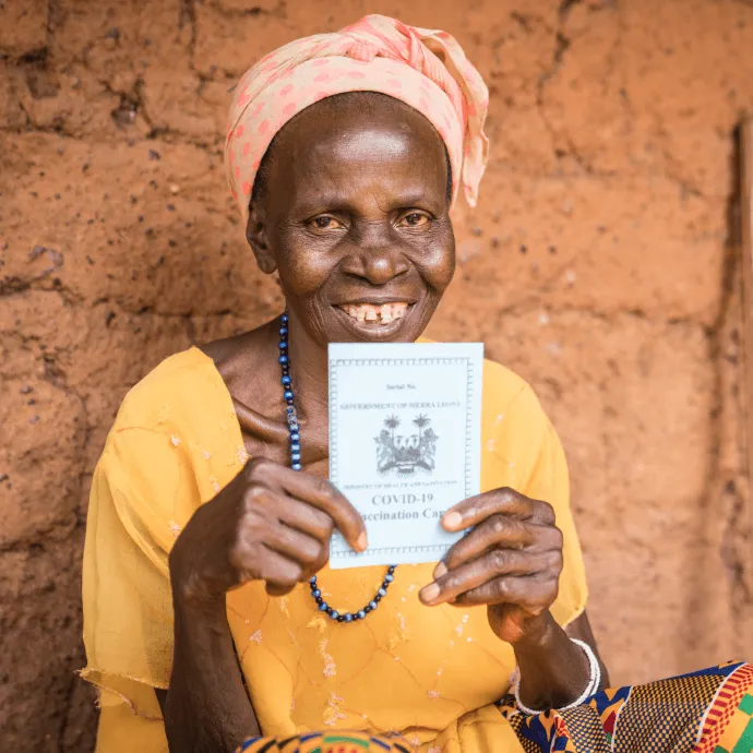 Sally sits outside her home holding her vaccine card after receiving her first dose of COVID-19 vaccine in Mansuthu.