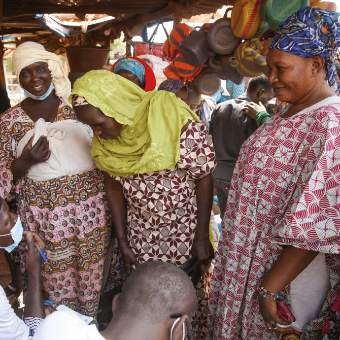 Market-goers and sellers, majority women of all ages and young men, queue to receive their first dose of COVID-19 vaccine for free.